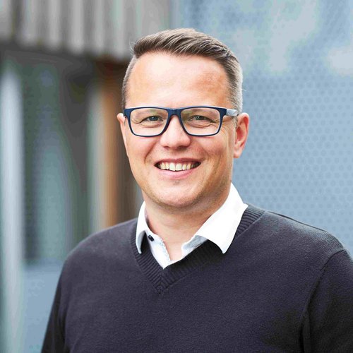 GP JOULE Mitarbeiter mit dunklem Pullover und weißem Hemd vor moderner Gebäudefassade.