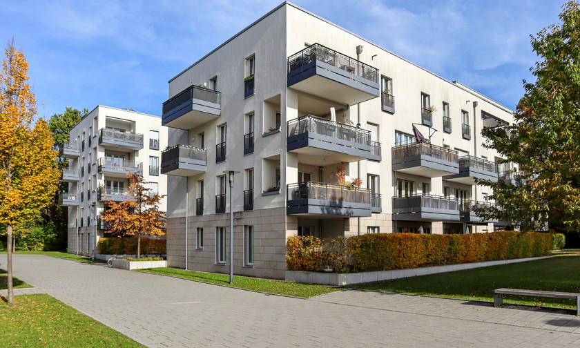 Mehrstöckige moderne Wohngebäude mit Balkonen, von herbstlichen Bäumen umgeben, an einem gepflasterten Gehweg gelegen.